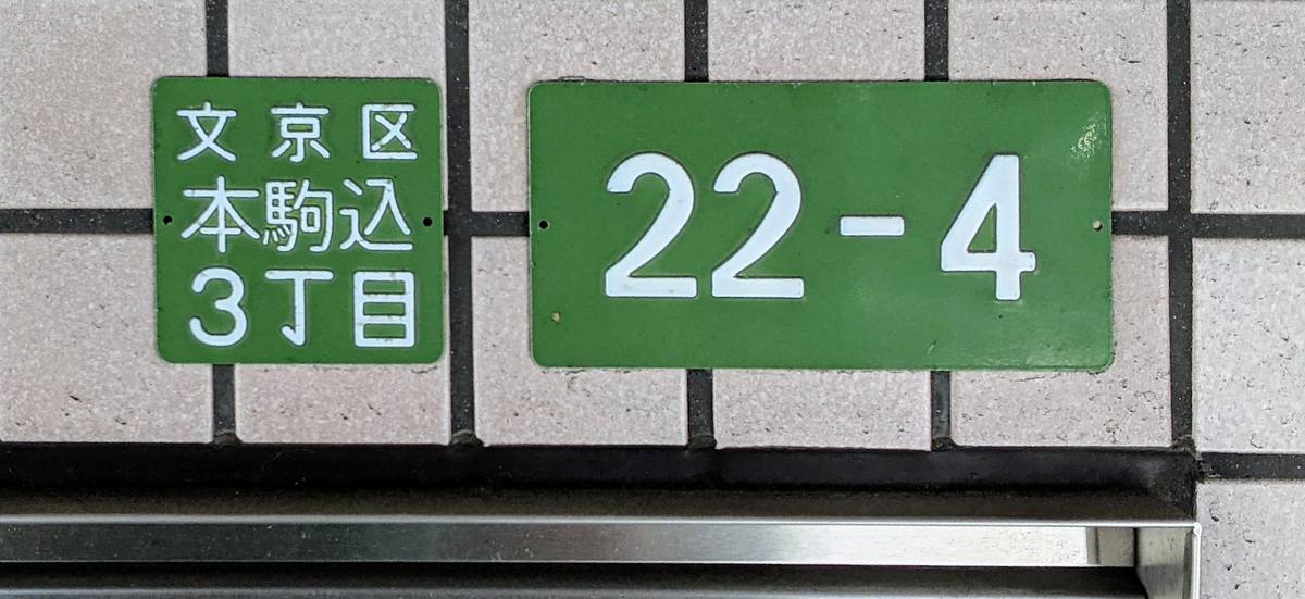 To grønne emaljeskilt på en flislagt husvegg, det ene med bydel og kvartalgruppe på japansk, det andre med de store tallene 22-4