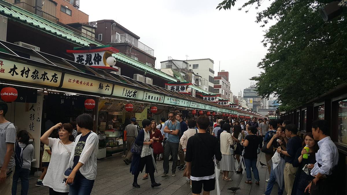 Nakamise-gaten i Asakusa full av folk mellom to rekker små butikker med grønne markiser og røde lykter, med Senso-jis tak i enden