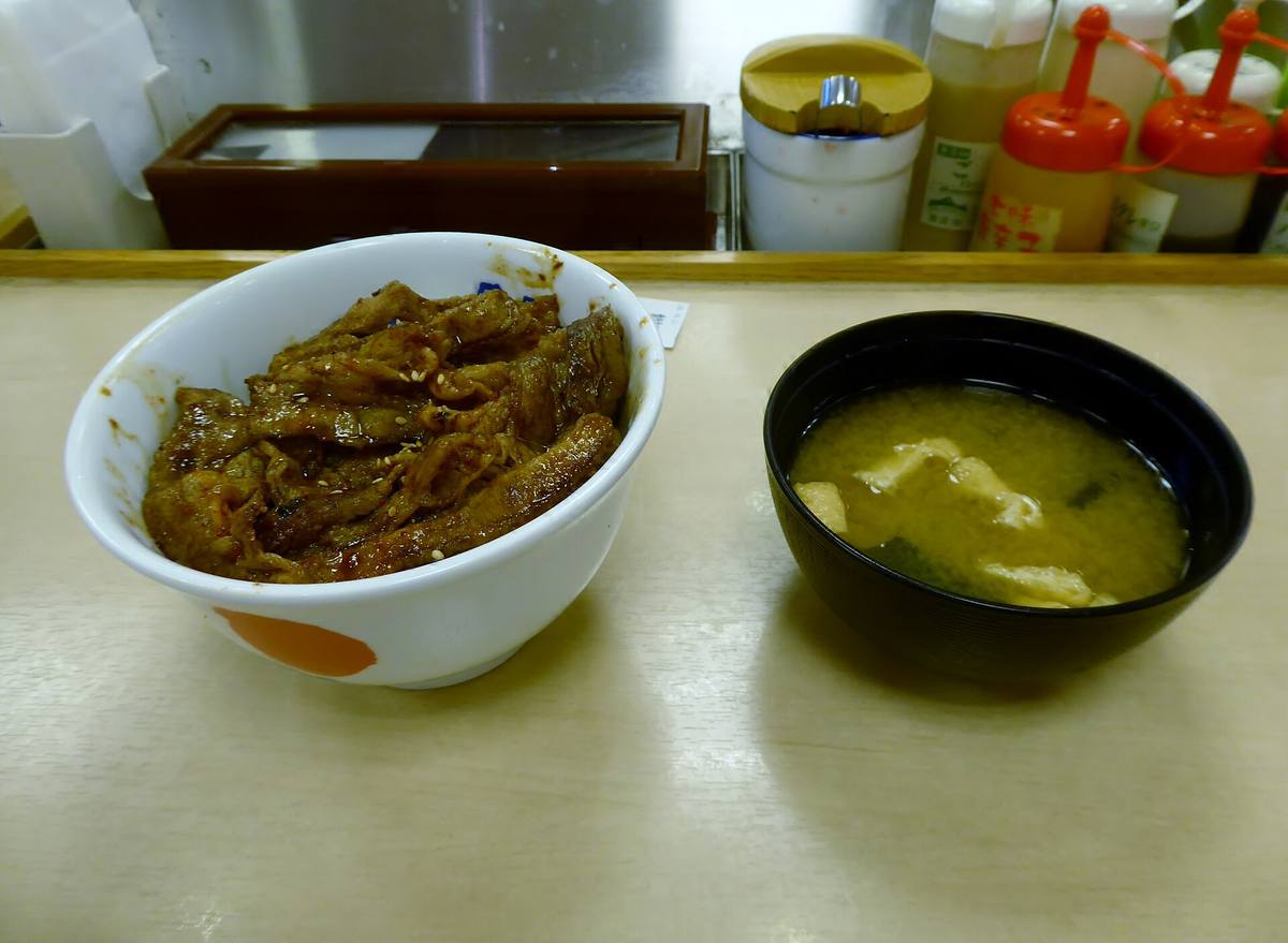 Risbolle med skiver av grillet kjøtt i mørk saus, servert med en skål misosuppe på en lys benkeplate