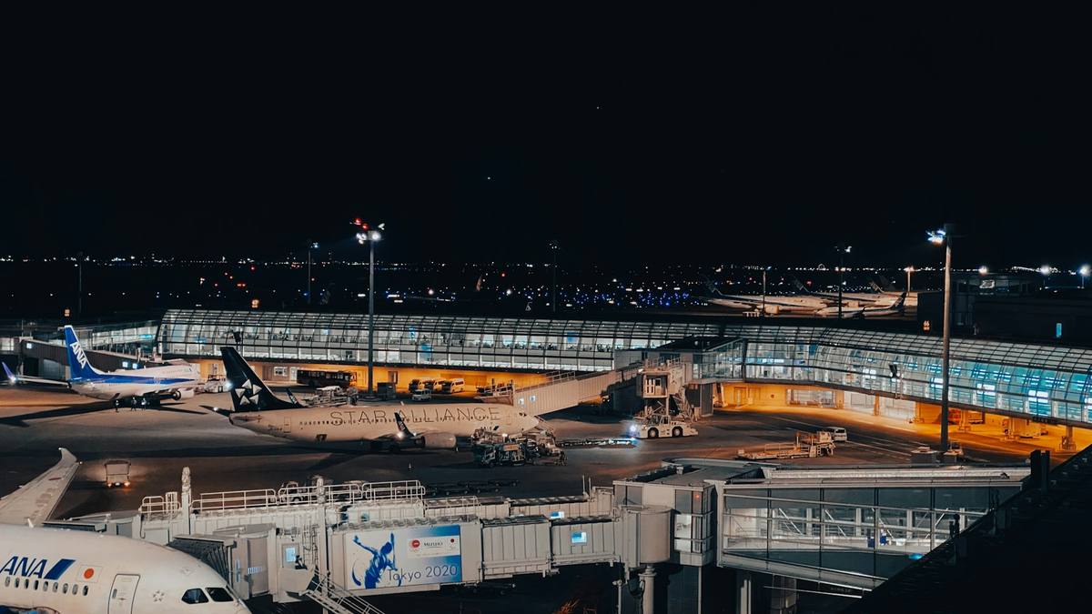 Fly ved gate på en japansk flyplass om kvelden, med opplyste terminalbroer og bakkemannskap på plassen