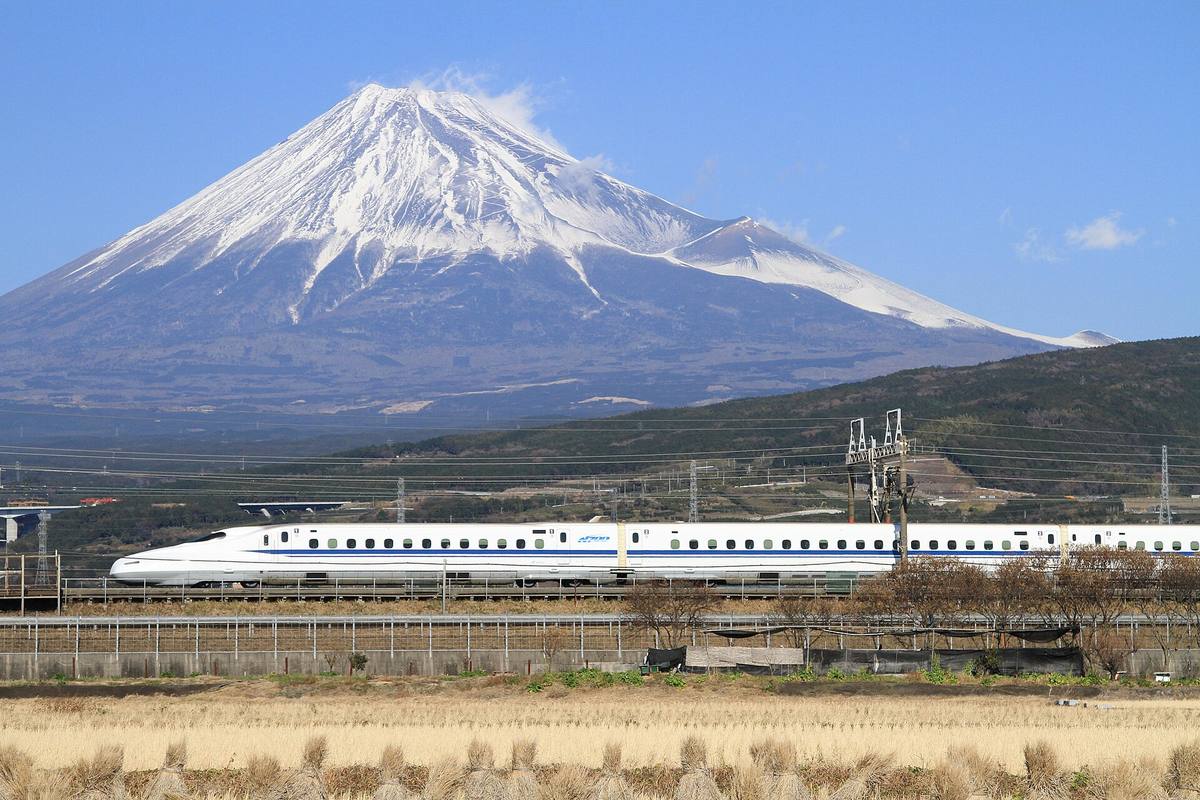 Hvit shinkansen av typen N700 på vei langs sporet med Fuji og snødekt topp rett bak