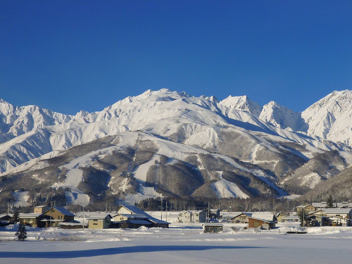 Snødekte fjell over Hakuba-dalen med skiløyper i fjellsiden og landsbyens tak i forgrunnen