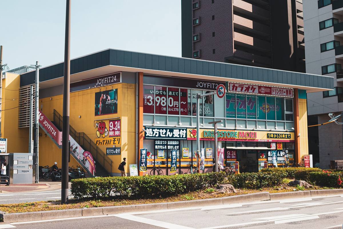 Fasaden på et japansk apotek med gule skilt, priser i store tall og et eget skilt for mottak av resepter ved inngangen
