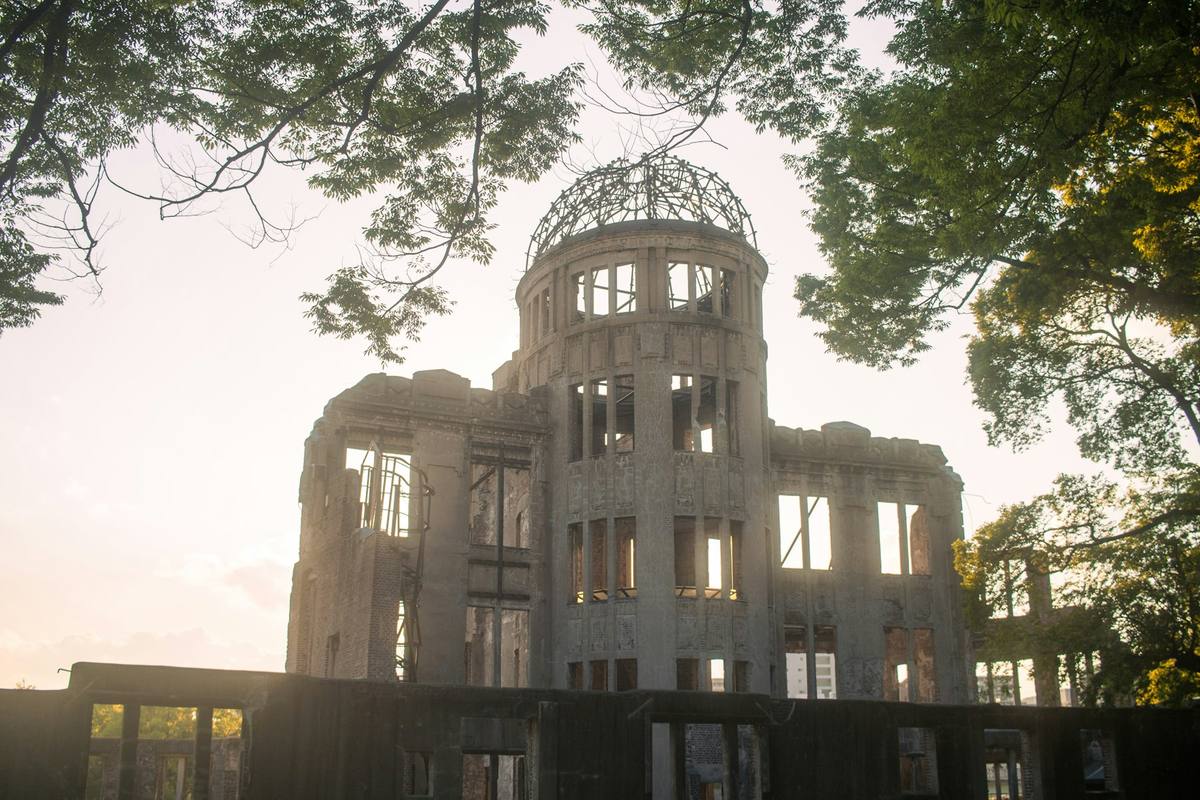 Ruinen av Atombombekuppelen med den bare stålrammen over kuppelen, sett gjennom løvverk i lavt kveldslys