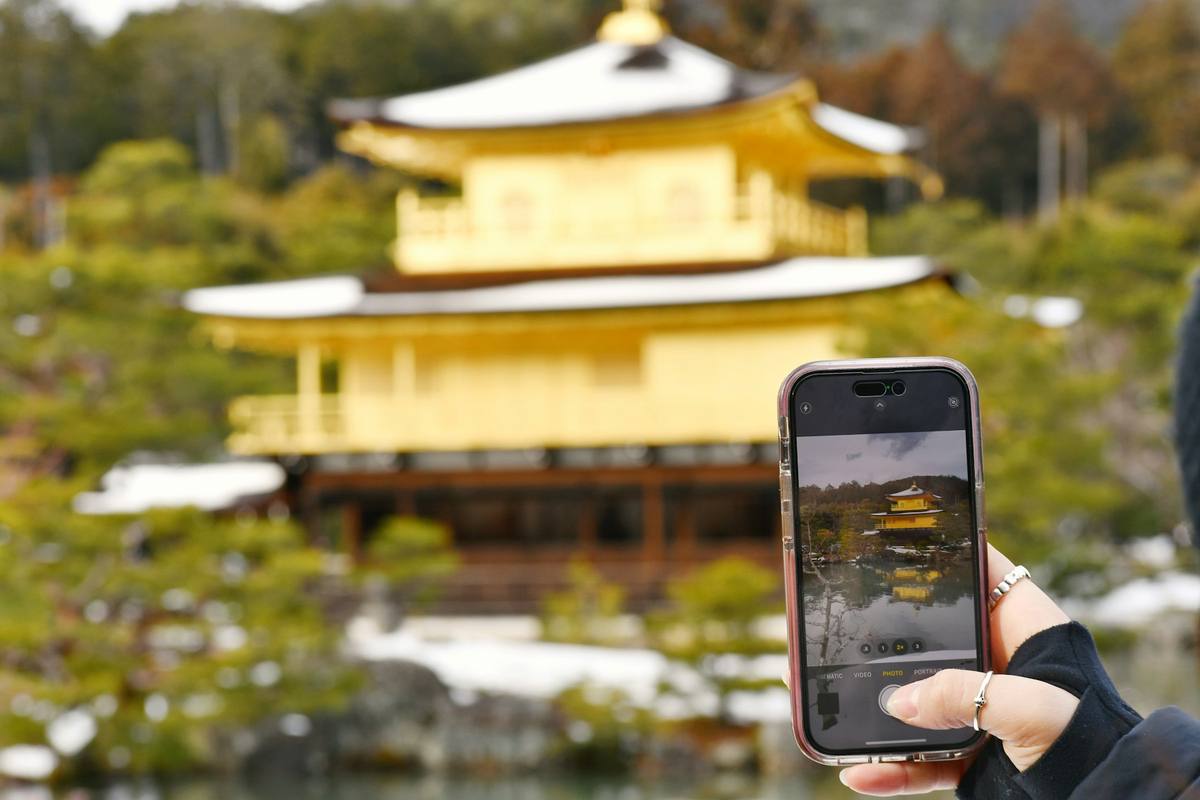 En hånd holder en smarttelefon opp foran et gyllent japansk tempel, og skjermen viser bygningen speilet i dammen