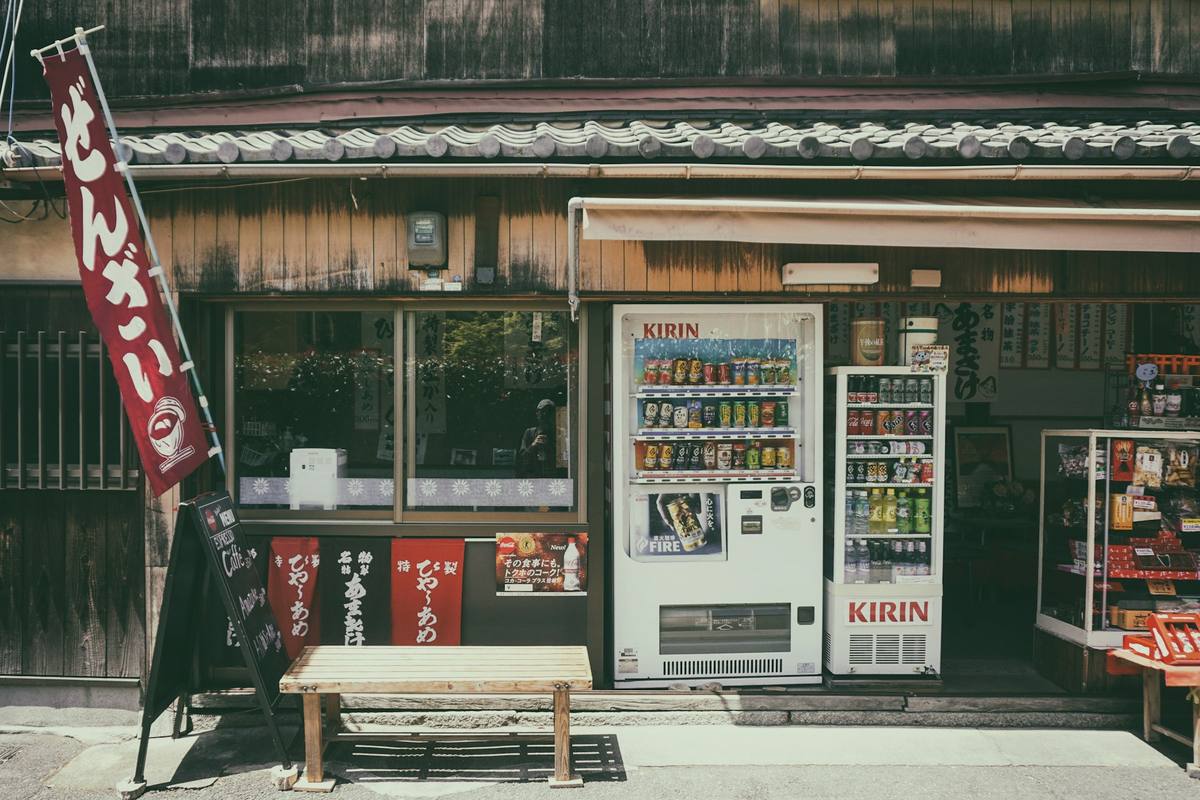 Gammel trefasade med en japansk drikkeautomat, kjøleskap med flasker og små prisskilt i yen på veggen ved siden av