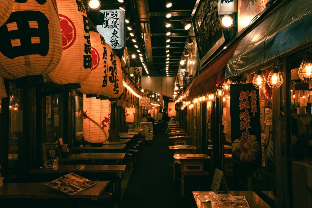 Trangt smug med røde papirlykter, trebenker og bord langs begge sider av små spisesteder om kvelden