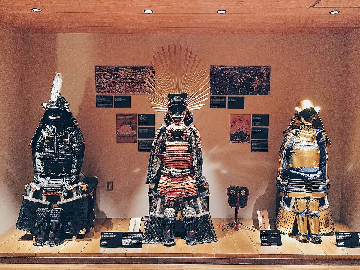 Tre komplette samurairustninger med hjelmer og ansiktsmasker utstilt i en glassmontre på museum