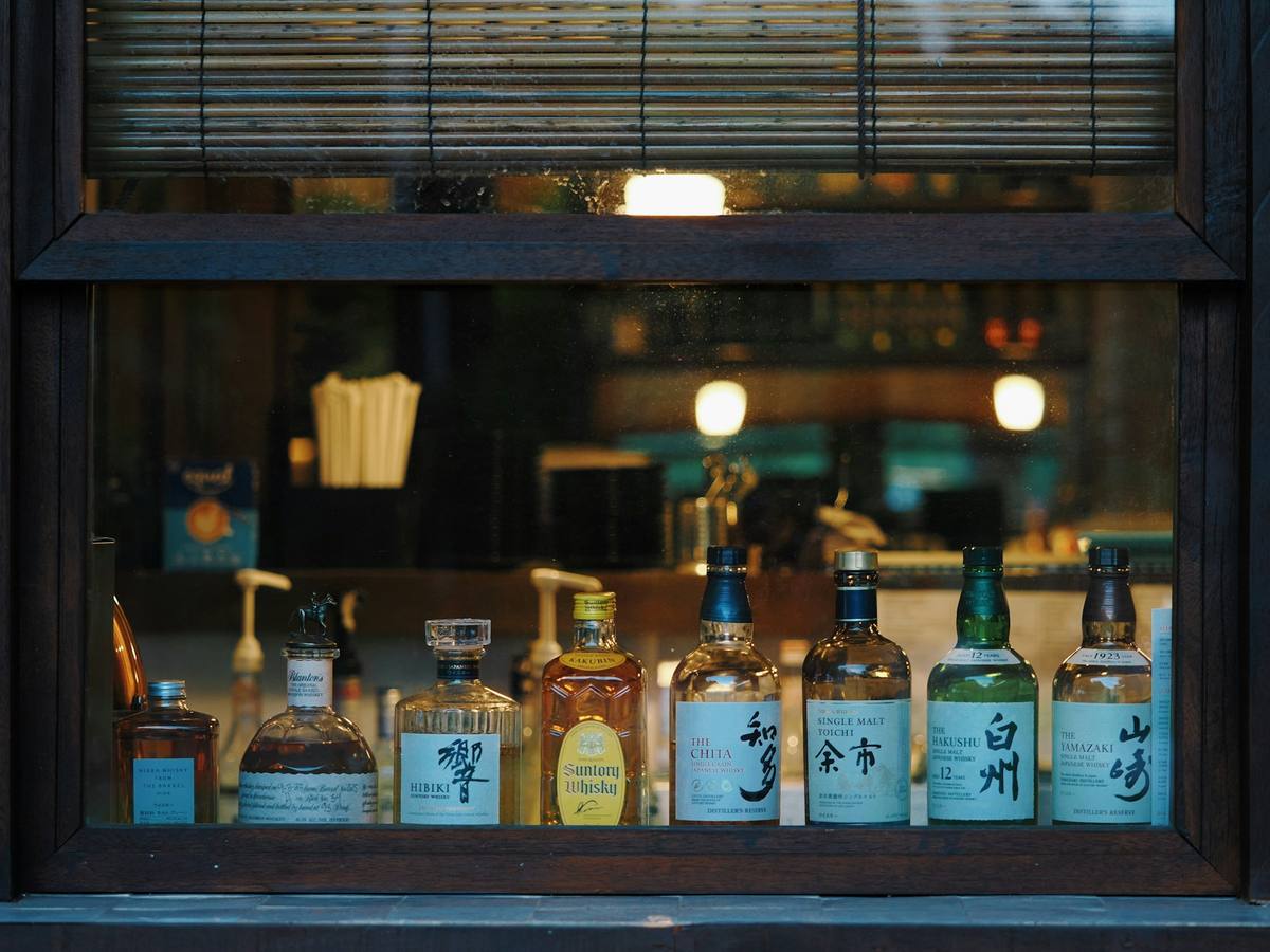 Rekke flasker japansk whisky i et vindu, blant dem Hibiki, Yamazaki, Hakushu, Yoichi og Chita, med et opplyst barlokale bak