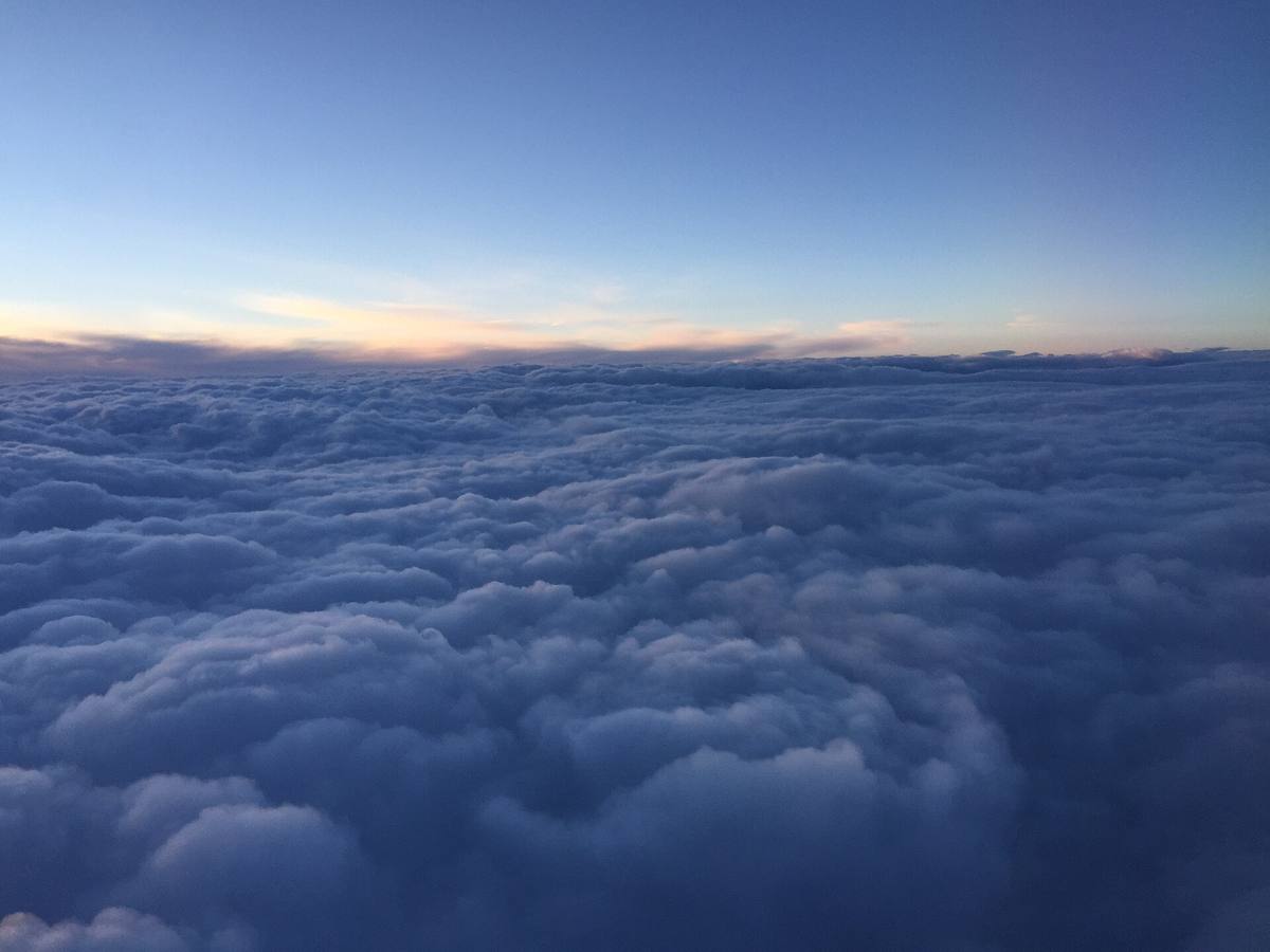 Utsikt fra flyvindu over et sammenhengende skydekke i daggry, med oransje og blå horisont