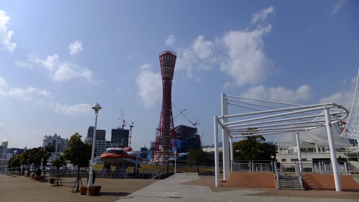 Det røde Kobe Port Tower ved havnepromenaden, med hvite stålkonstruksjoner og skyer over
