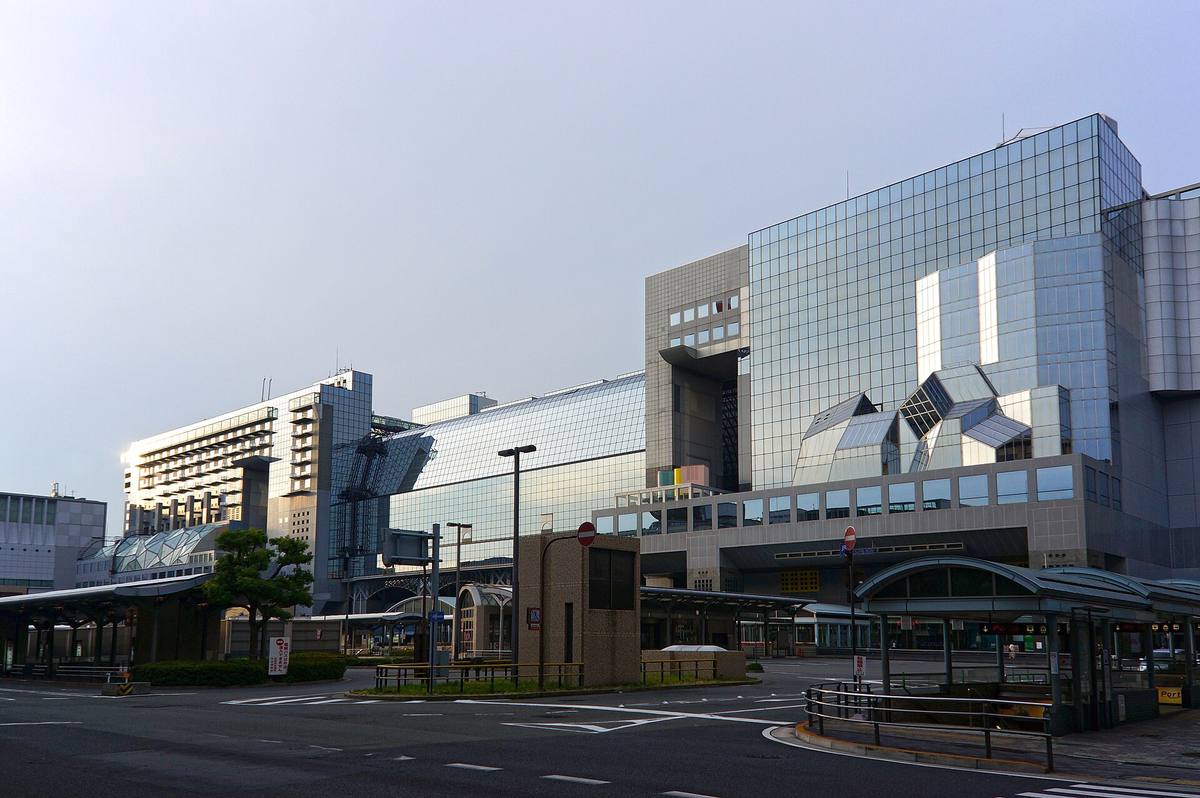 Kyoto stasjons store glass- og betongfasade med skrå takflater sett fra bussterminalen på plassen utenfor