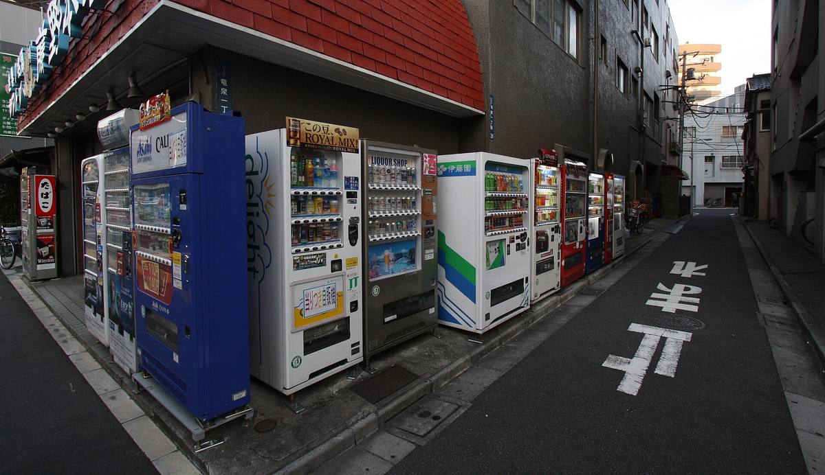 En lang rekke drikke- og tobakksautomater stilt opp langs husveggen i en smal japansk sidegate