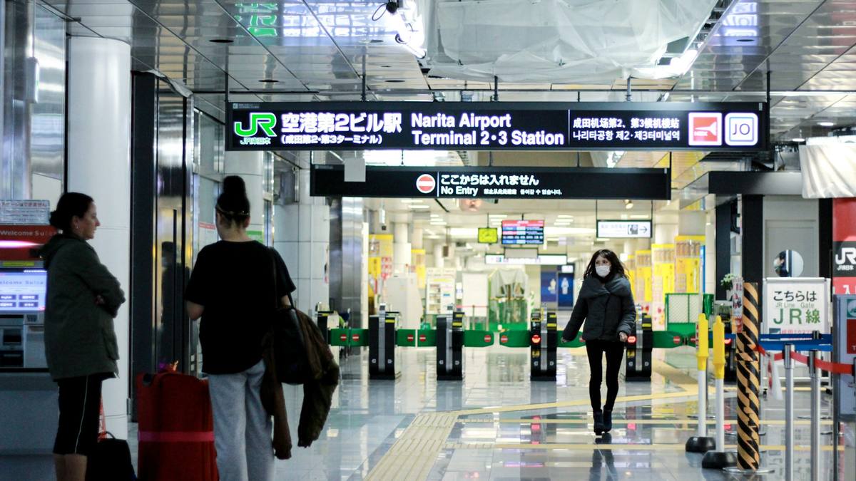 Opplyst JR-skilt for togstasjonen ved Narita terminal 2 og 3, med billettsperrer og reisende med kofferter i ankomsthallen
