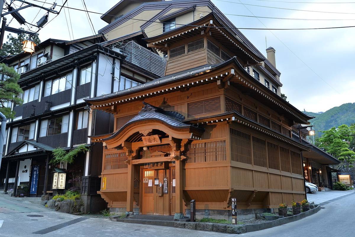 Det store trebadehuset Oyu på et gatehjørne i Nozawa Onsen, med svungent tak, sprossevegger og opplyst inngang i skumringen