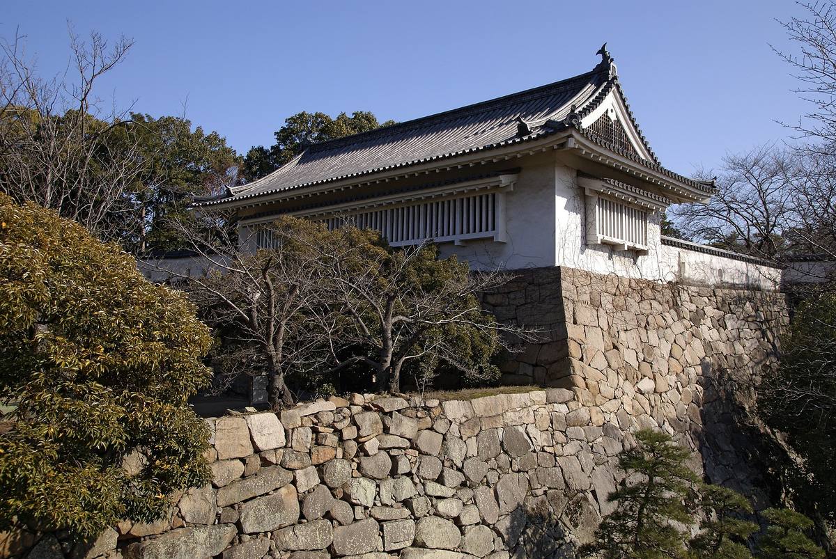 Tsukimi-yagura, det bevarte hvitkalkede vakttårnet på Okayama-slottet, reist på en høy mur av ubearbeidede steinblokker med bare trær rundt