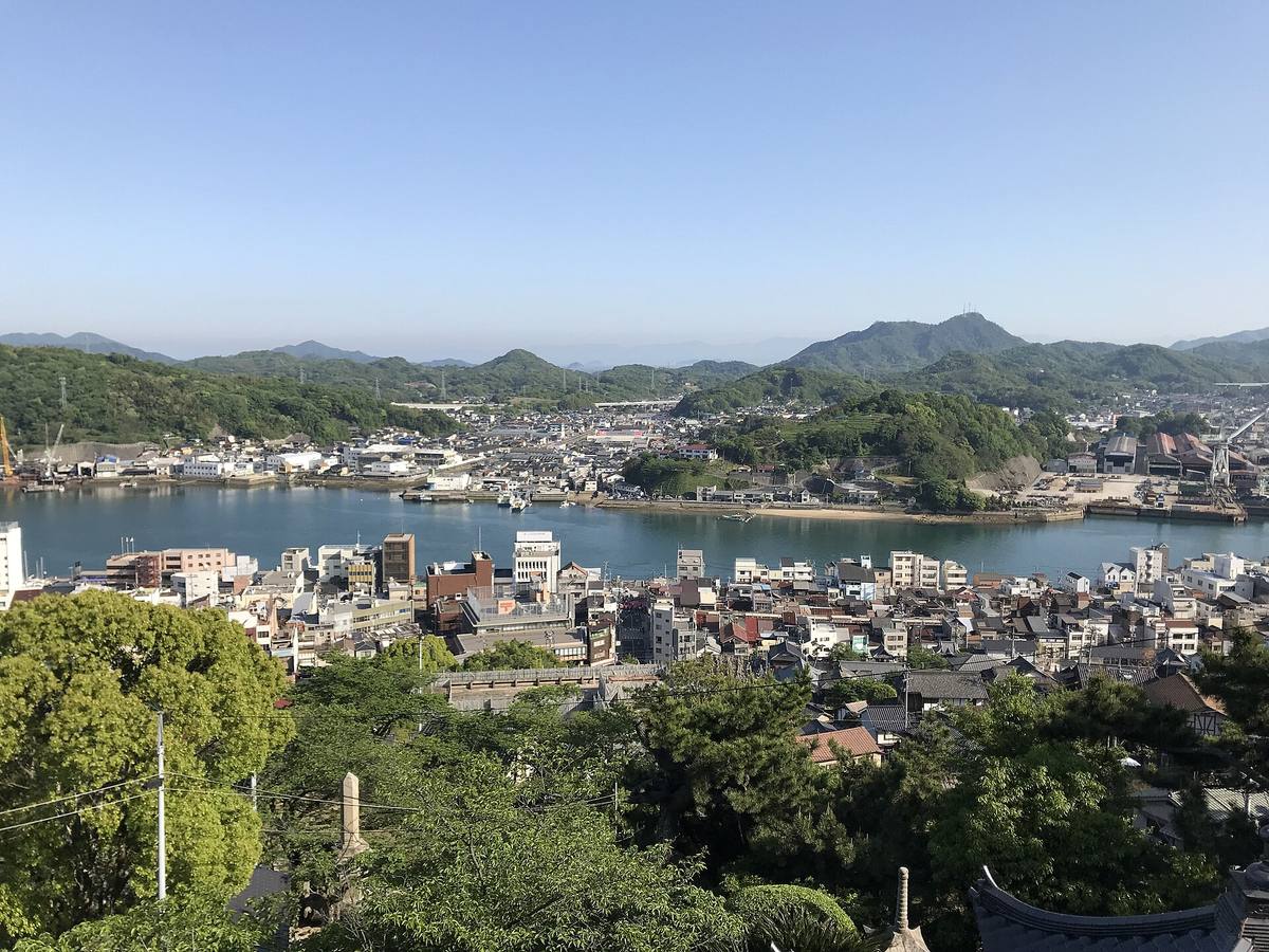 Utsikt over Onomichi-sundet fra åsen, med byens tak langs vannet og grønne fjell på motsatt side