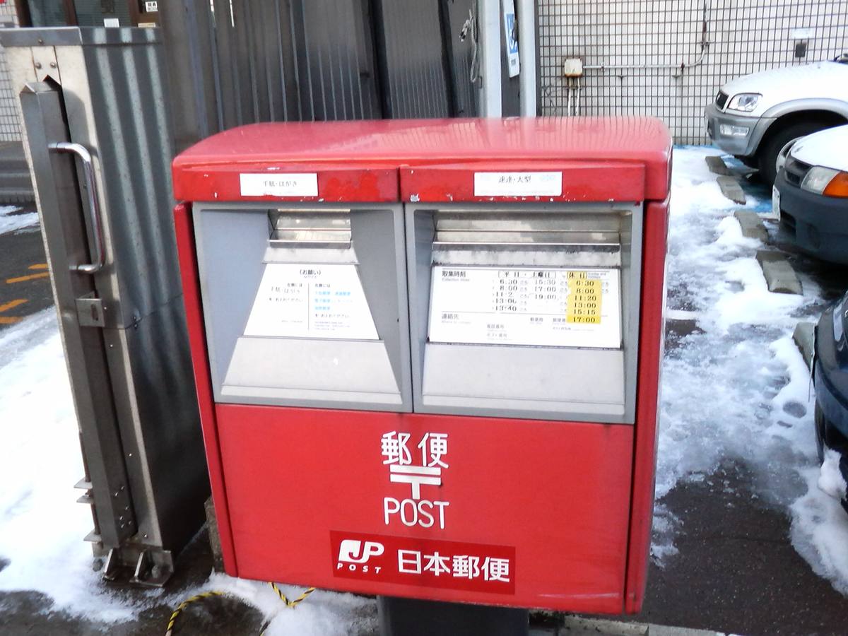 Rød japansk postkasse med to innkast og tømmetider på japansk, merket Japan Post, i snø