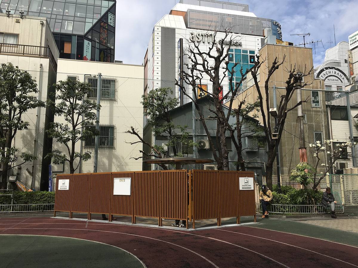Avgrenset røykeområde ute på en japansk gate, skjermet med trelameller og med skilt om reglene