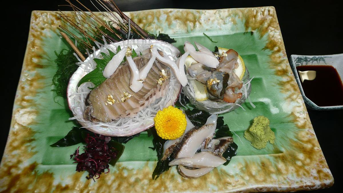Sashimi av abalone anrettet på perlemorskjell og revet reddik på et grønt keramikkfat, med wasabi og en skål soyasaus ved siden av