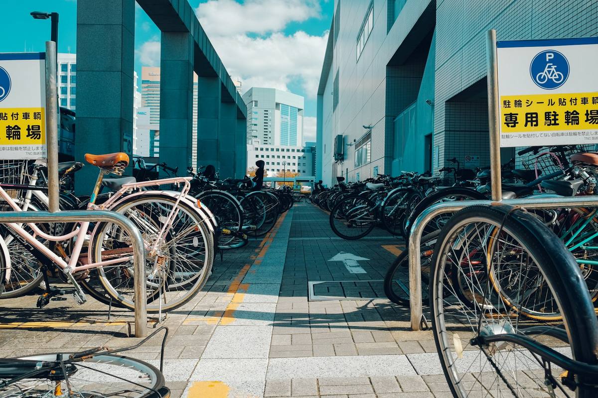 Tette rader med sykler med kurv på en regulert sykkelparkering, med blå parkeringsskilt med sykkelsymbol og gule tavler med japansk tekst