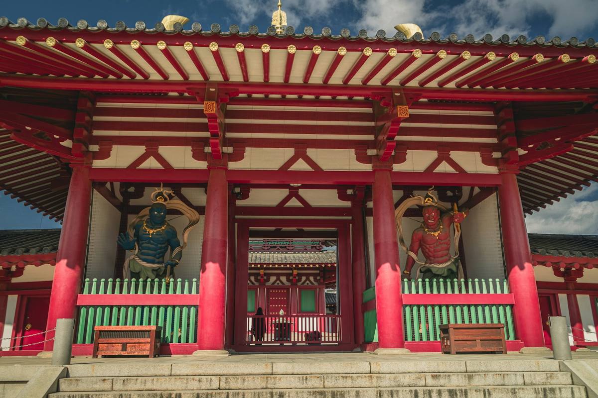 Buddhistisk tempelport i rødt tre med tegltak, der en blå og en rød vaktfigur står i hver sin åpning på hver side av inngangen