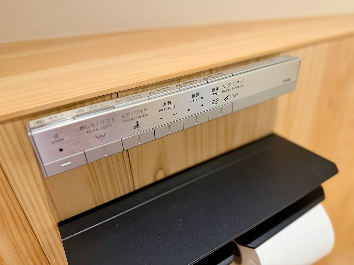 Betjeningspanel til japansk washlet montert på en trevegg, med japanske og engelske knappetekster for spyling, vannstyrke, posisjon og tørking