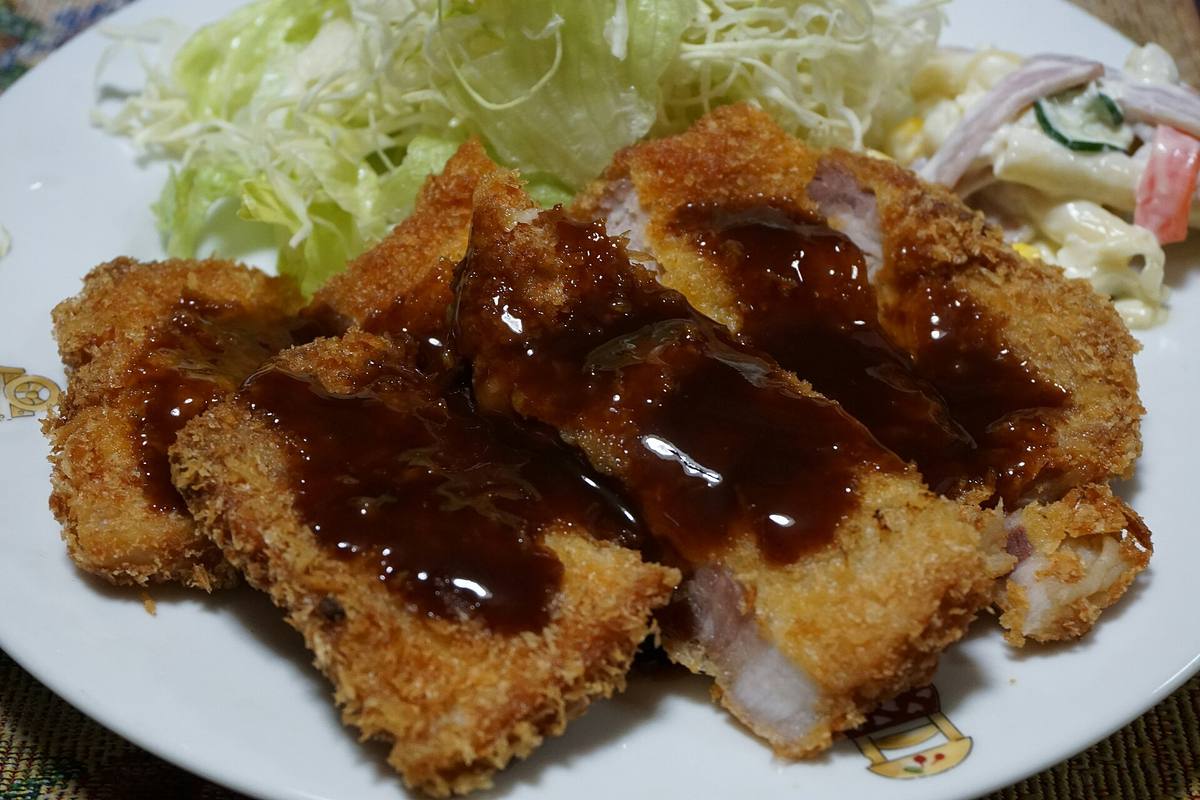 Oppskåret panert svinekotelett med brun saus, finstrimlet kål og potetsalat på en hvit tallerken