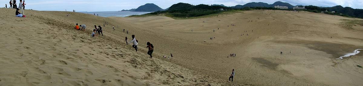 Vidstrakte sandklitter som bølger ned mot havet, med små menneskeskikkelser spredt utover sandflaten