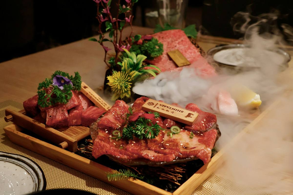 Trebrett med rått wagyu-kjøtt i skiver der den kraftige marmoreringen er tydelig, anrettet med grønn pynt og damp fra tørris