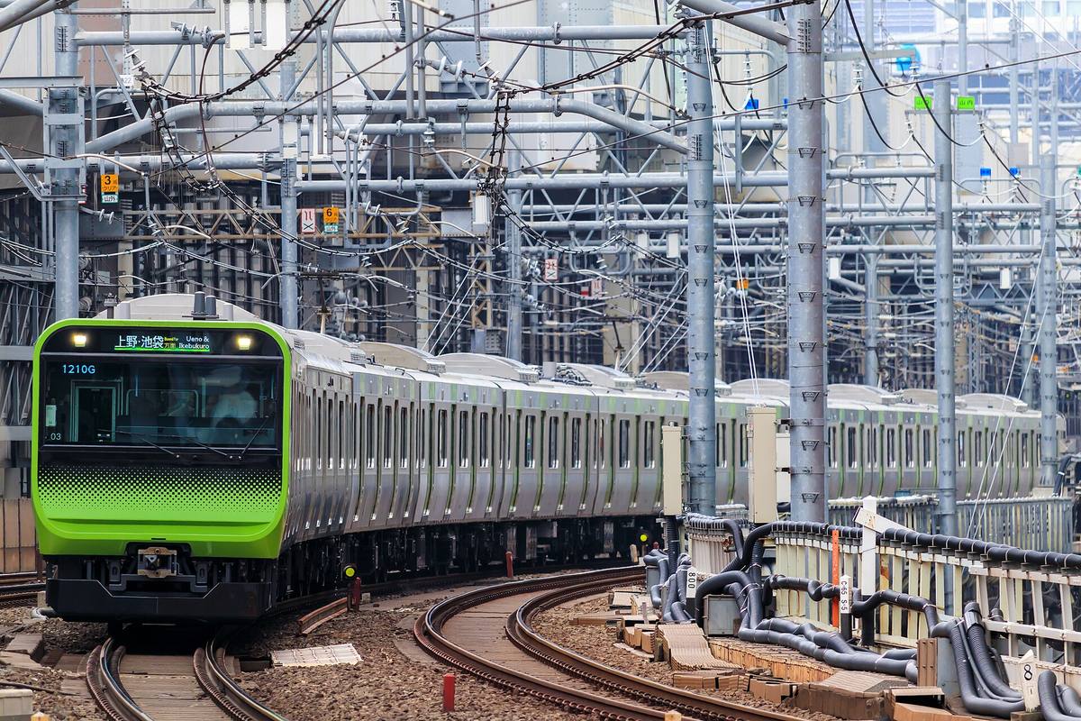 Tog på Yamanote-linjen med sitt grønne beltestrøk i en sving, under et tett nett av kjøreledninger